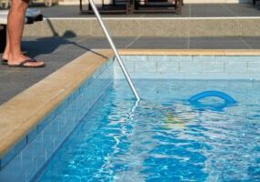 Male cleaning outdoor swimming pool with underwater vacuum tube
