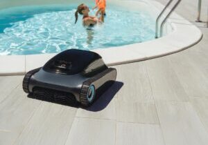 A robotic pool cleaner on the poolside with a mother and child enjoy swimming in clear blue water on background . Modern pool maintenance cleaning convenience.